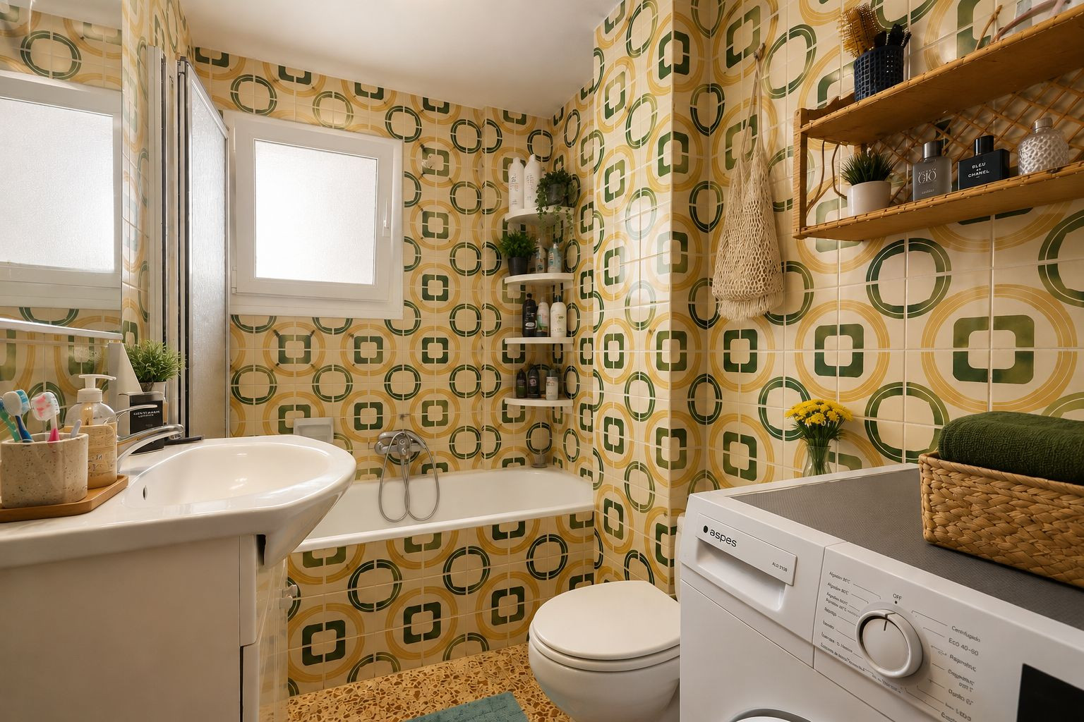 The full bathroom features distinctive yellow and green geometric patterned tiles, a white vanity with sink, a bathtub with shower screen, and an integrated washing machine, illuminated by a frosted window.