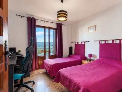 Bright bedroom featuring two single beds with fuchsia headboards and direct balcony access offering mountain views. Includes a desk area and terrazzo flooring.