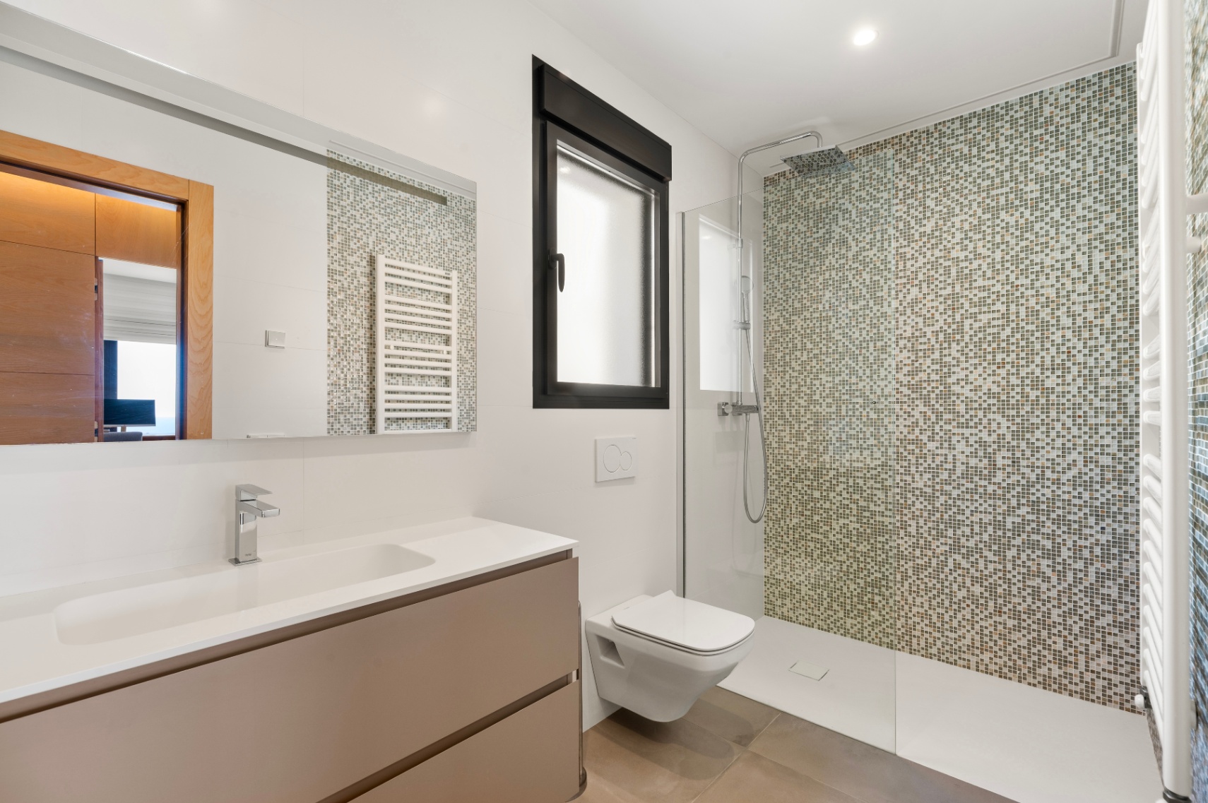 Modern bathroom featuring a walk-in shower with a mosaic tiled wall in earthy tones. It includes a floating vanity with an integrated sink, a wall-mounted toilet, and a black-framed window.