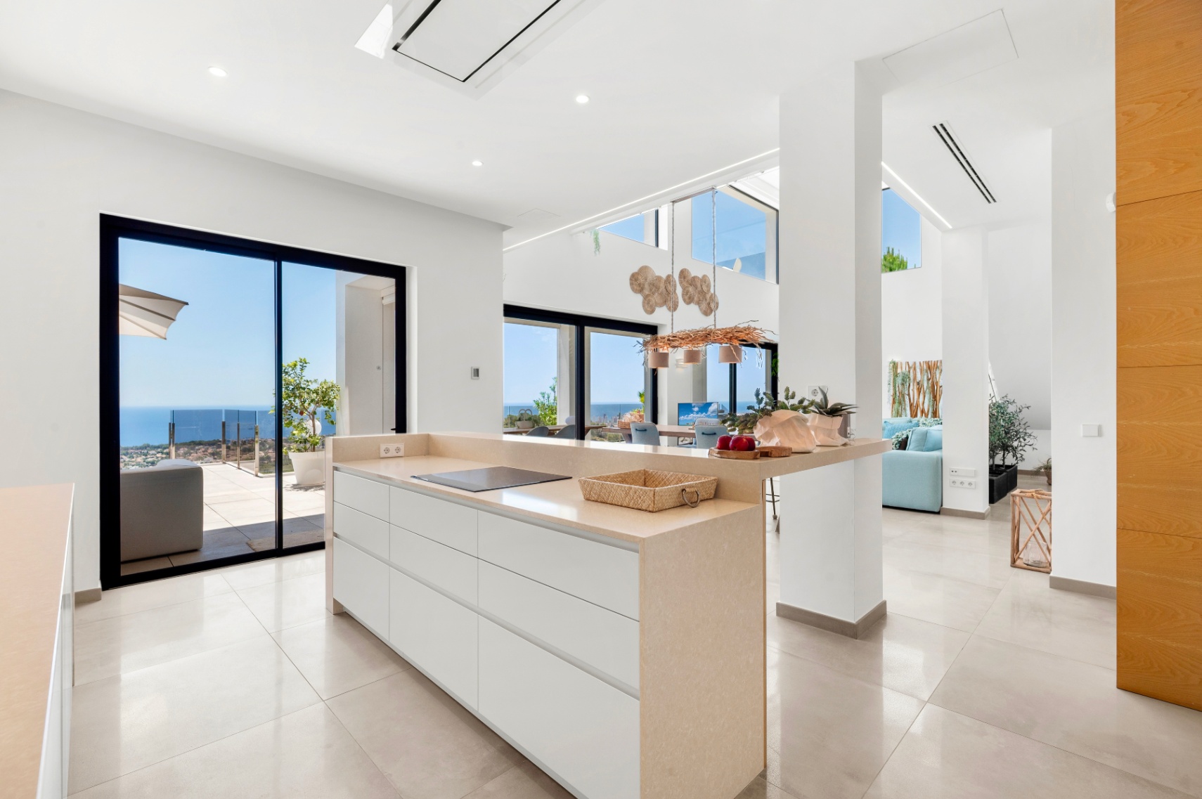 Modern open-plan kitchen featuring a central island with a beige countertop and integrated induction hob. Expansive sliding glass doors provide direct Mediterranean sea views, enhancing the bright, contemporary space.