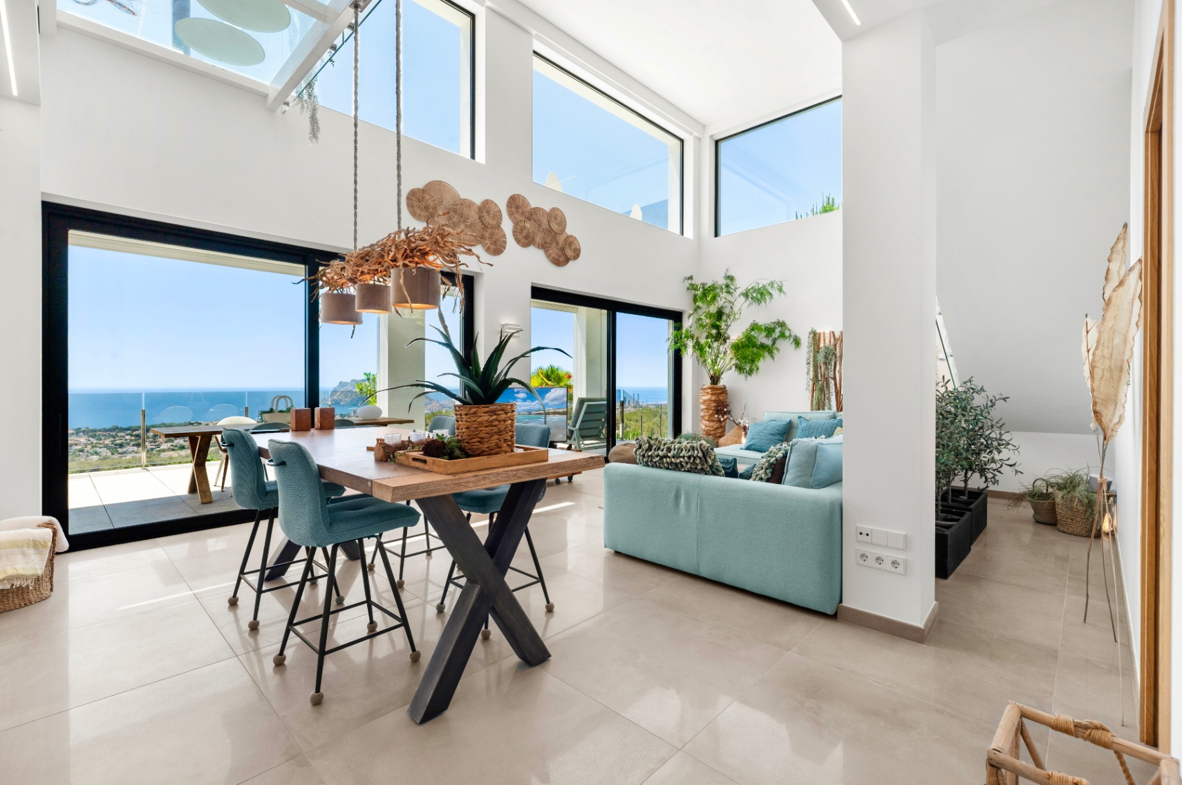 Spacious open-plan living and dining area featuring high ceilings, large windows, and a unique branch chandelier. Enjoy panoramic sea views of the coastline and Peñon de Ifach from the light-filled interior.