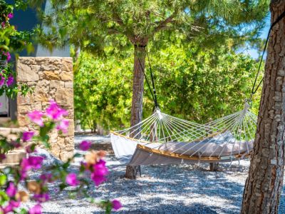 A tranquil garden corner featuring a comfortable grey hammock with wooden spreader bars, suspended between trees on a gravel bed, framed by vibrant bougainvillea.