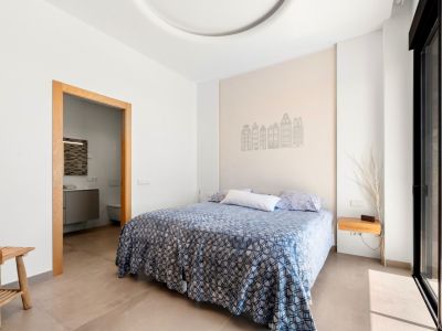 Bright bedroom featuring a double bed, an accent wall with building silhouettes, and a wooden-framed doorway to an en-suite bathroom. Direct access to a terrace via a large sliding glass door.