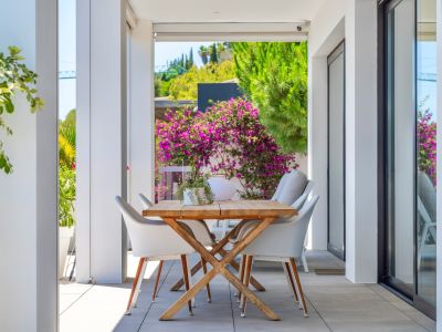 Covered outdoor dining terrace with a wooden table and white chairs, framed by lush greenery and vibrant bougainvillea, perfect for al fresco meals.