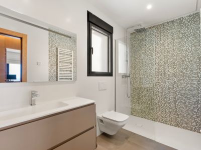 Modern bathroom featuring a walk-in shower with a mosaic tiled wall in earthy tones. It includes a floating vanity with an integrated sink, a wall-mounted toilet, and a black-framed window.
