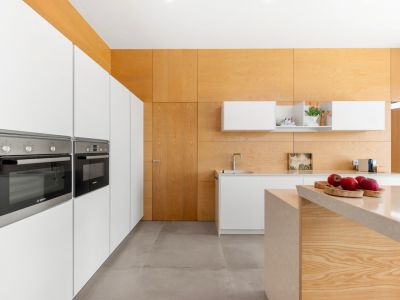 Modern kitchen featuring integrated white cabinetry with Bosch ovens. A central island with a light stone countertop and light wood paneling on walls and ceiling define the space.