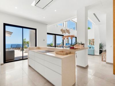 Modern open-plan kitchen featuring a central island with a beige countertop and integrated induction hob. Expansive sliding glass doors provide direct Mediterranean sea views, enhancing the bright, contemporary space.
