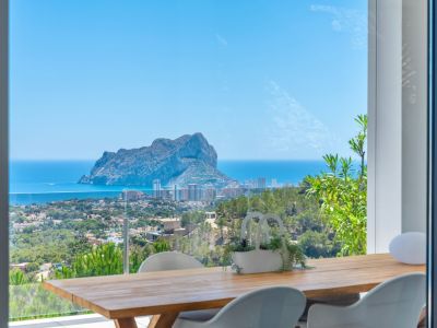 Outdoor dining terrace featuring a wooden table and modern white chairs, offering panoramic views of Peñon de Ifach, the Mediterranean Sea, and Calpe's coastline.
