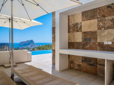 Outdoor terrace with a built-in counter featuring multi-toned natural stone-look tiles. Offers panoramic sea views, an infinity pool, and the iconic Peñon de Ifach.