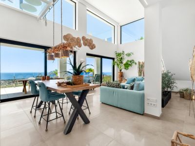 Spacious open-plan living and dining area featuring high ceilings, large windows, and a unique branch chandelier. Enjoy panoramic sea views of the coastline and Peñon de Ifach from the light-filled interior.