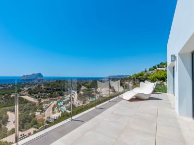 Spacious outdoor terrace featuring light-toned tiles, a modern white lounge chair, and a clear glass balustrade. Enjoy panoramic views of the Mediterranean Sea, the iconic Peñón de Ifach, and the Calpe coastline.