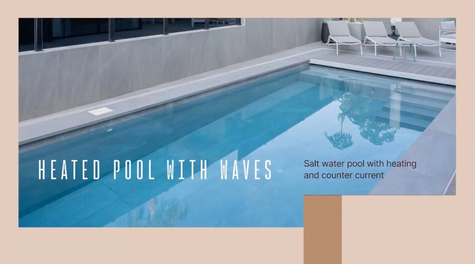 Heated salt water pool with counter-current system and steps, bordered by grey tiling and a sun deck with lounge chairs.