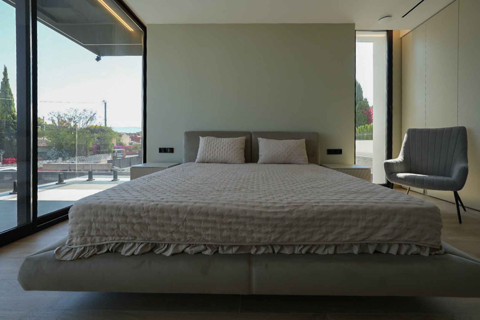 Master bedroom with a floating bed, upholstered headboard, expansive windows offering sea views, and an armchair. Integrated bedside tables.
