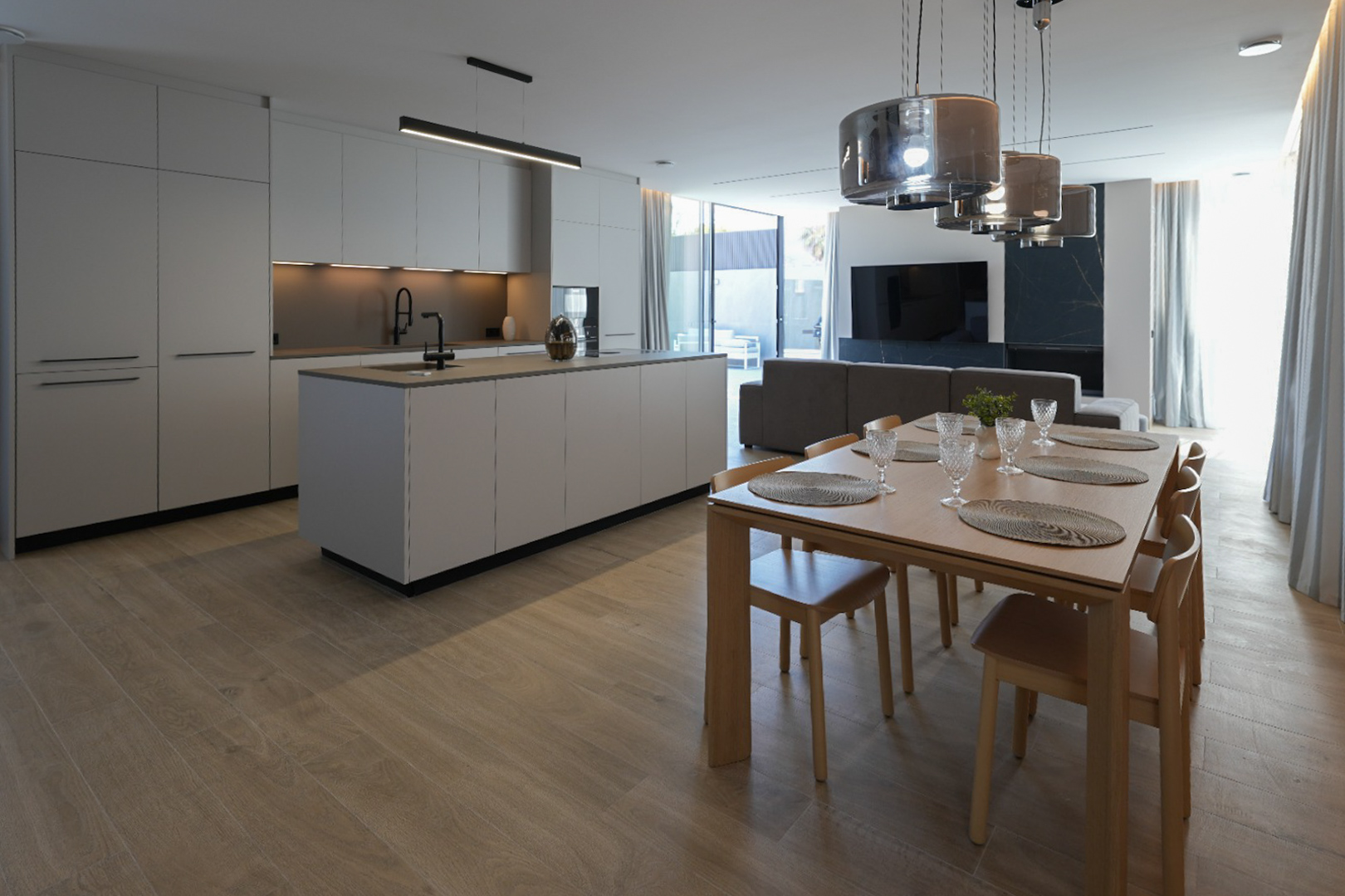 Minimalist design kitchen with a central island and black faucet, open to an elegant wooden dining area with six chairs and modern pendant lights.
