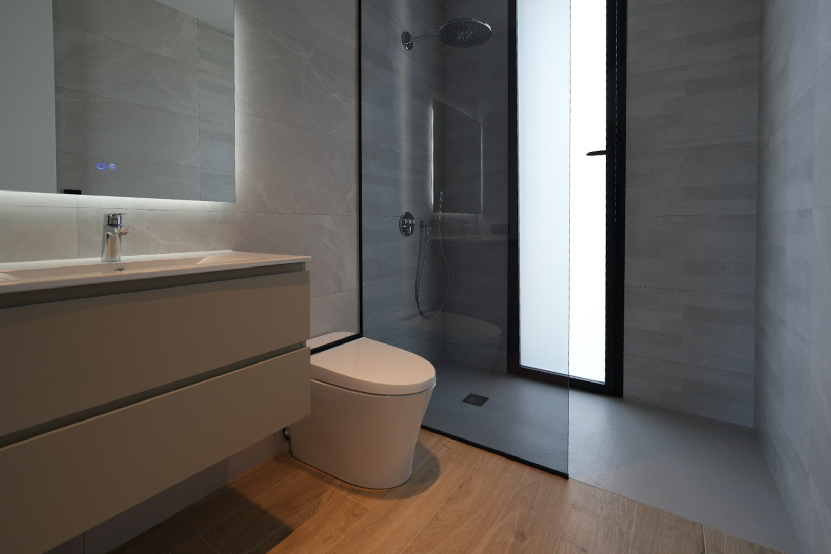Modern bathroom featuring a floating vanity, illuminated mirror, wall-mounted toilet, and a walk-in shower with rain head, all complemented by grey tiled walls and wood-effect flooring.