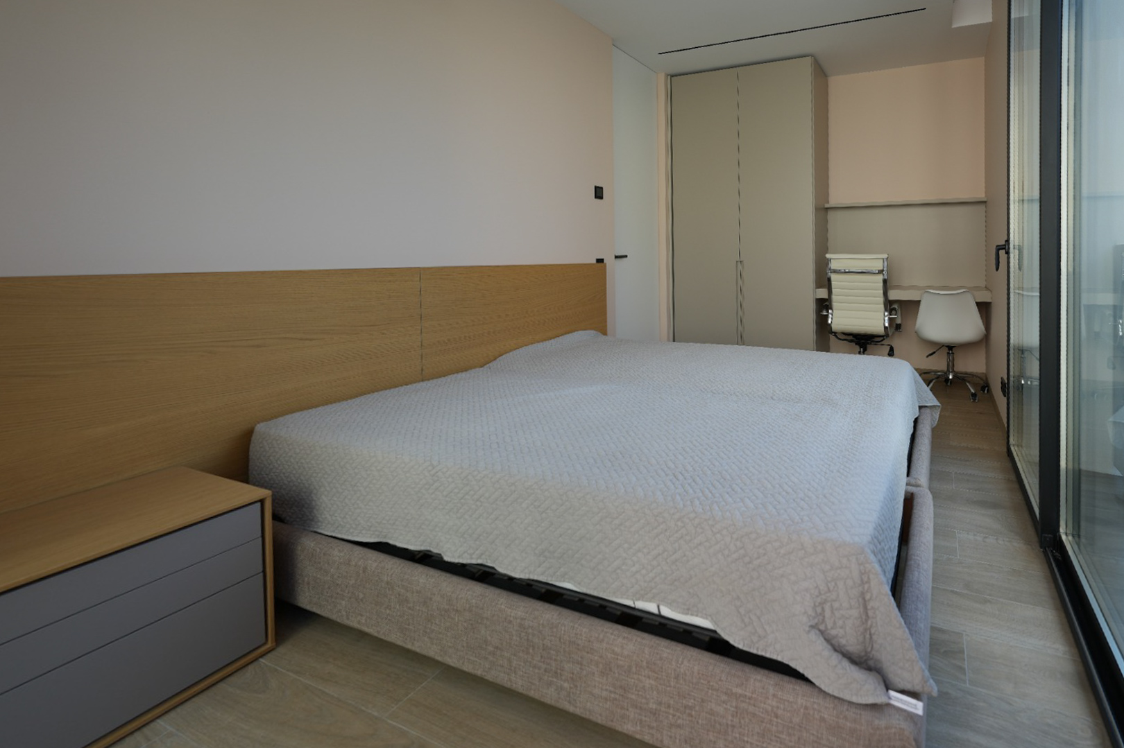 Modern bedroom featuring a light grey upholstered bed with a wooden headboard and integrated bedside table. Includes a built-in wardrobe, double desk area, and large glass doors.