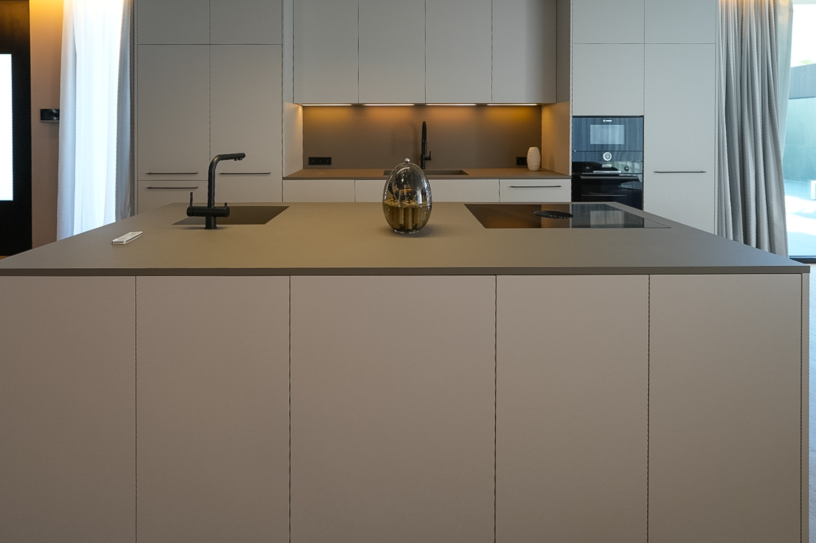 Modern kitchen featuring a central island with integrated sink, induction hob, and sleek neutral-toned cabinetry.
