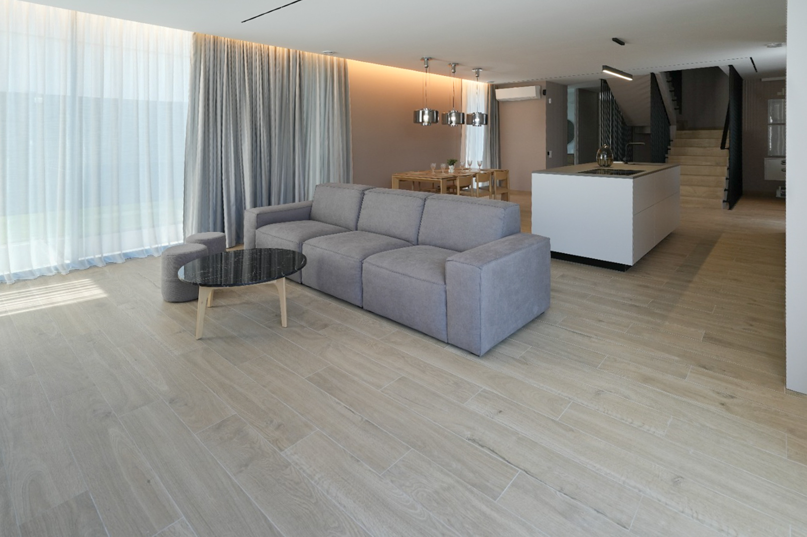 Open-plan living room featuring a grey modular sofa, black marble coffee table, and wood-look tiled floor. Large windows with sheer and grey curtains.