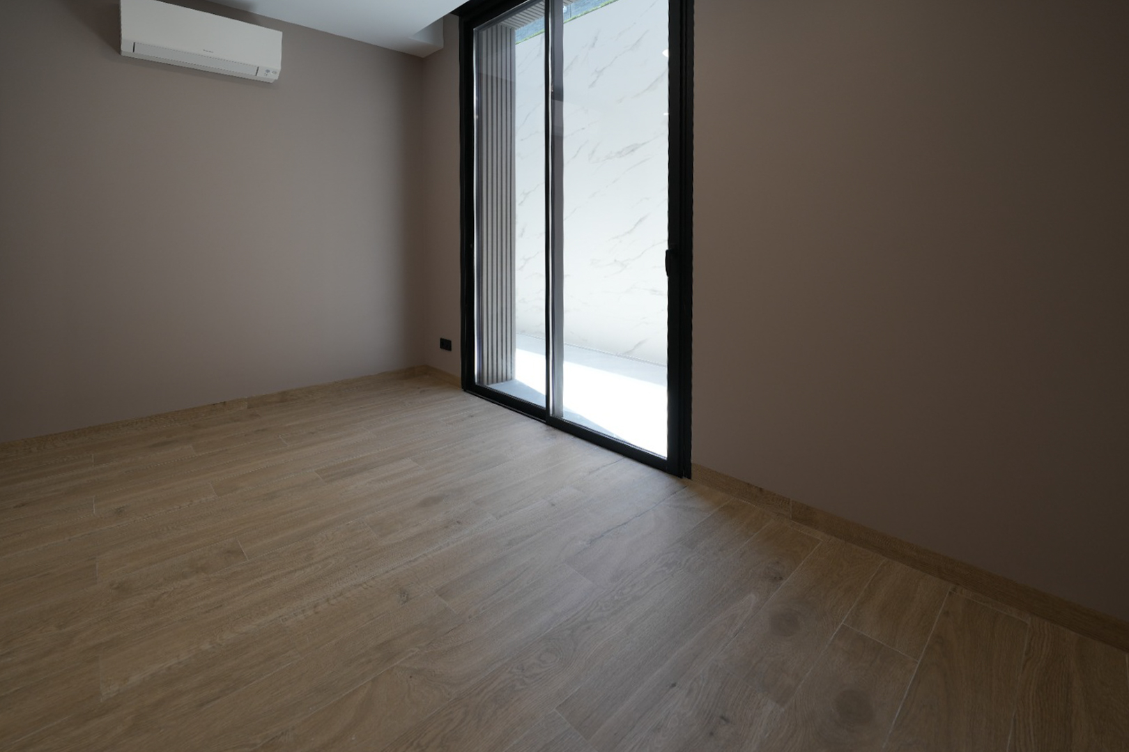 Unfurnished room with light wood-look tile flooring, taupe walls, and a black-framed sliding glass door. A wall-mounted AC unit is visible.