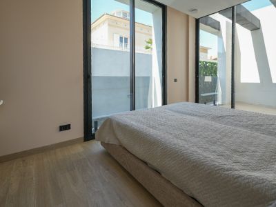 Bright bedroom featuring light wood flooring and expansive black-framed sliding glass doors, opening to an outdoor area with views of a neighboring house and green wall.