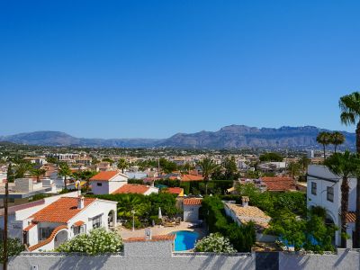 Elevated view of the Albir residential area, featuring a private pool, houses with tiled roofs, and lush Mediterranean greenery, with mountains in the background.