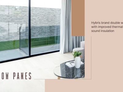 Expansive black-framed double-glazed windows overlook a textured grey stone wall and green lawn, brightening a modern interior featuring light flooring and a marble-top coffee table.