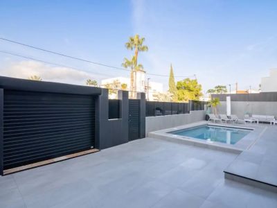 Exterior view showcasing the private pool, light grey tiled patio, and secure dark grey garage door with pedestrian gate.