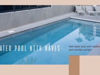 Heated salt water pool with counter-current system and steps, bordered by grey tiling and a sun deck with lounge chairs.