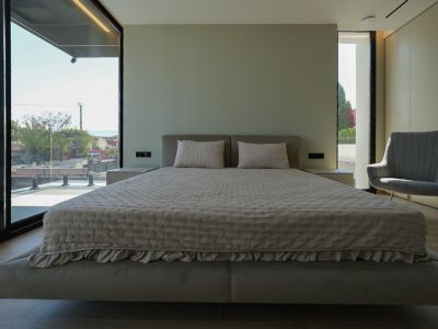 Master bedroom with a floating bed, upholstered headboard, expansive windows offering sea views, and an armchair. Integrated bedside tables.