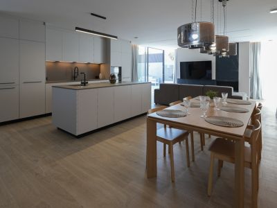 Minimalist design kitchen with a central island and black faucet, open to an elegant wooden dining area with six chairs and modern pendant lights.