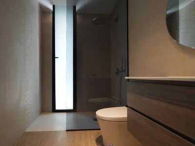 Modern bathroom featuring a wooden vanity, round mirror, and walk-in shower. Textured wall tiles and a frosted window provide light.