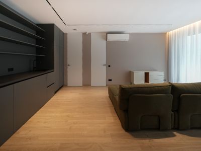 Modern living space featuring a dark grey integrated kitchenette, light wood-look flooring, and a green modular sofa. Flush doors and natural light.