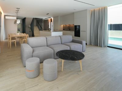 Open-plan living and dining area featuring a modular sofa, marble coffee table, integrated kitchen, and large windows overlooking the outdoor pool.