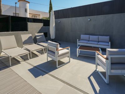 Outdoor terrace featuring modern lounge furniture in white and grey, with mixed porcelain tile and composite decking. Sun loungers and a sofa set are visible.