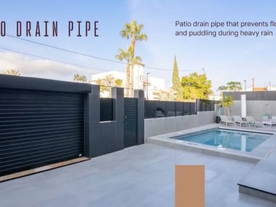 Spacious outdoor patio featuring a swimming pool, light grey tiled flooring, and a modern black garage door. Integrated patio drain pipe prevents water accumulation.