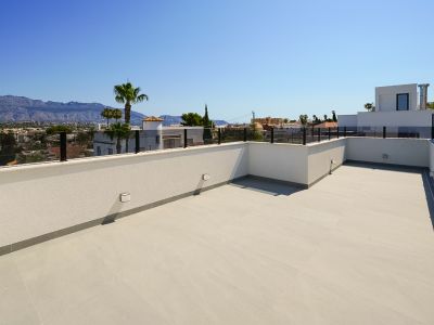 Spacious rooftop terrace with light-toned floor tiles and modern glass railing, offering panoramic views of distant mountains and the surrounding town.