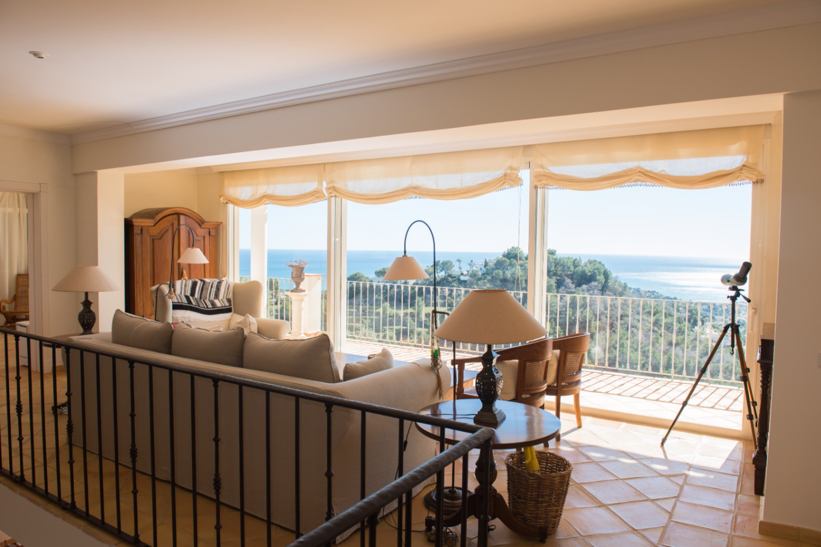 Bright living area featuring terracotta flooring, wrought iron railings, and large windows showcasing panoramic Mediterranean Sea and coastal views.