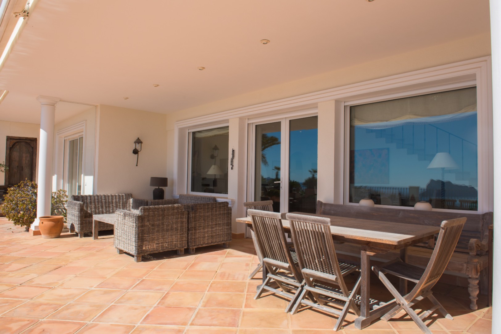 Covered terrace featuring terracotta tiling, a wooden dining set, and wicker lounge seating under a recessed lighting ceiling.