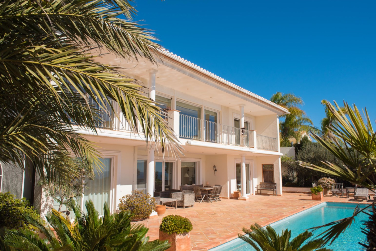 Exterior view of the two-story villa showing the terracotta terrace, private pool, and upper balcony with white columns and metal railings.