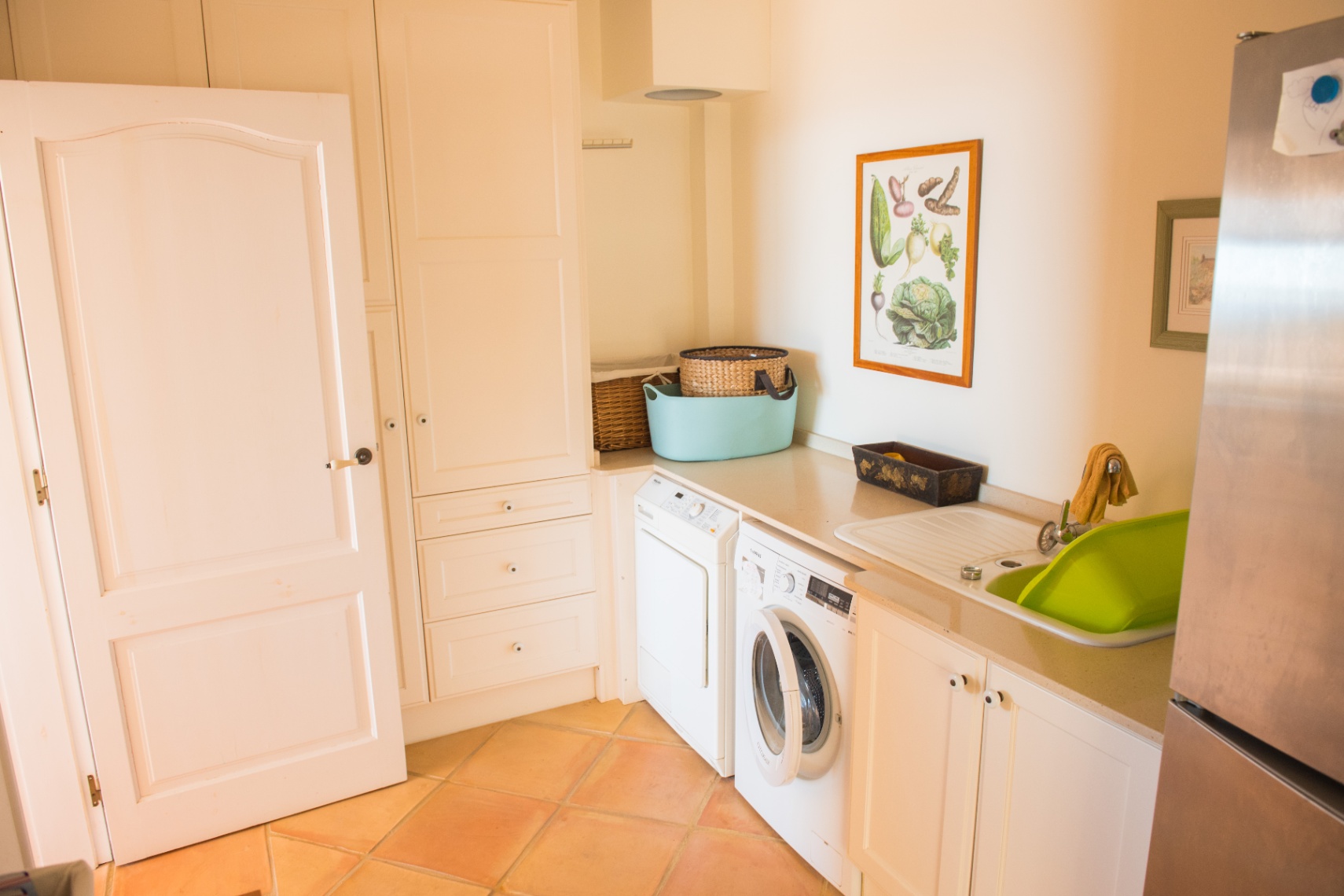Functional utility room equipped with custom white cabinetry, laundry appliances, and traditional terracotta tile flooring.