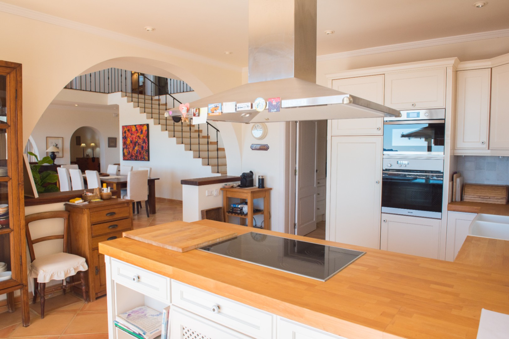 Open-plan kitchen featuring a wooden island with induction hob, stainless steel extractor, and integrated Miele ovens, overlooking the dining area.