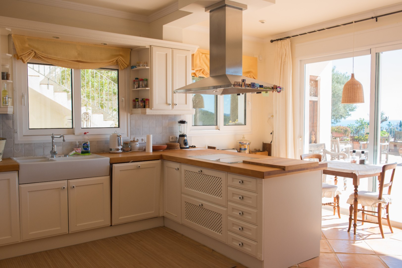 Rustic-style kitchen featuring white cabinetry, solid wood countertops, a ceramic farmhouse sink, and a stainless steel hood with direct terrace access.