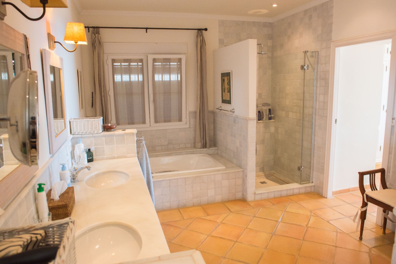 Spacious bathroom featuring a double marble vanity, terracotta tile flooring, a built-in bathtub, and a separate walk-in shower with glass enclosure.