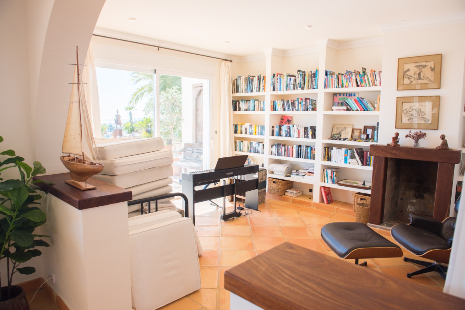 Spacious study area featuring a large built-in library, terracotta tile flooring, a fireplace with a wooden mantel, and direct access to the terrace.