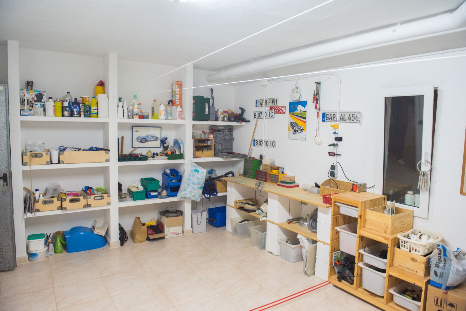 Spacious workshop and storage area featuring built-in masonry shelving, a wooden workbench, and tiled flooring for maintenance and hobby projects.