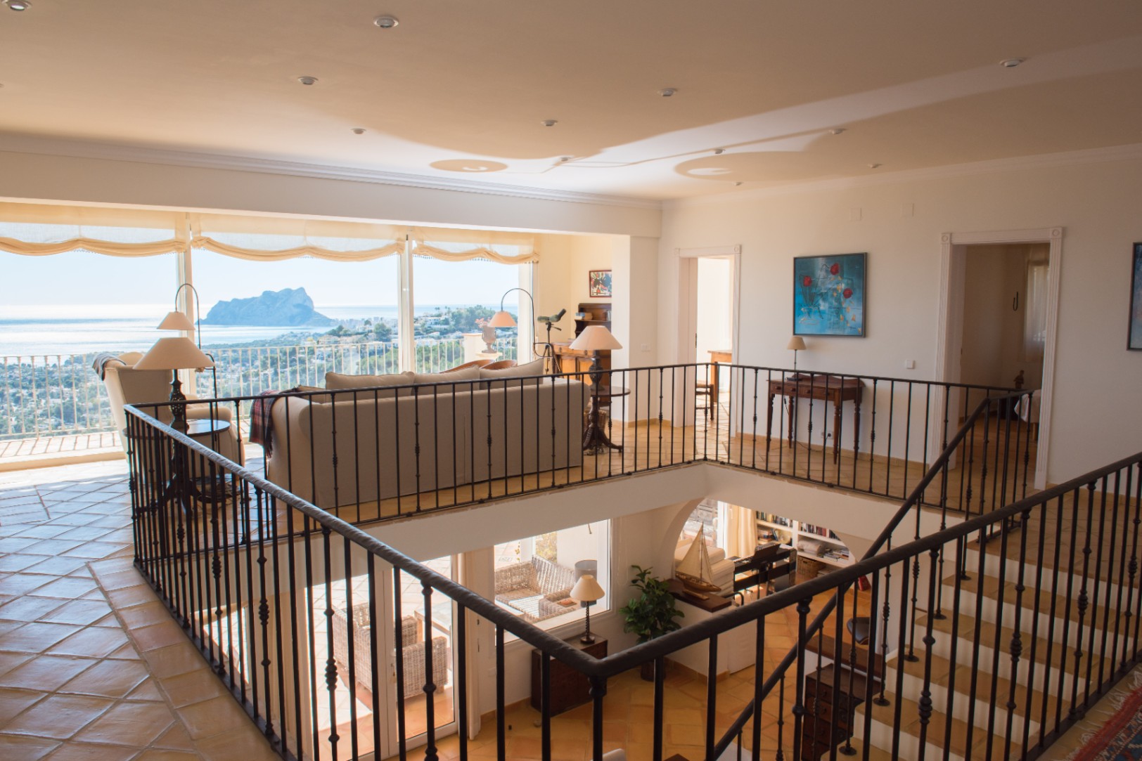 Upper-level living area featuring wrought iron railings, terracotta flooring, and large windows overlooking the Mediterranean Sea and Peñón de Ifach.