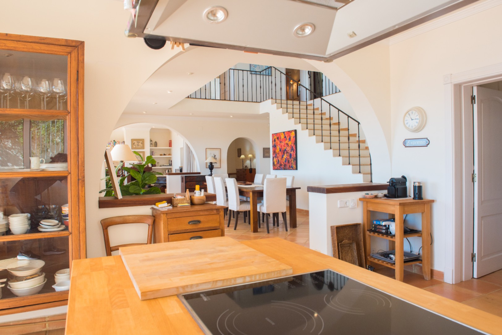 View from the kitchen island with wooden countertop towards the dining area and staircase, featuring traditional Mediterranean arches and tiled flooring.