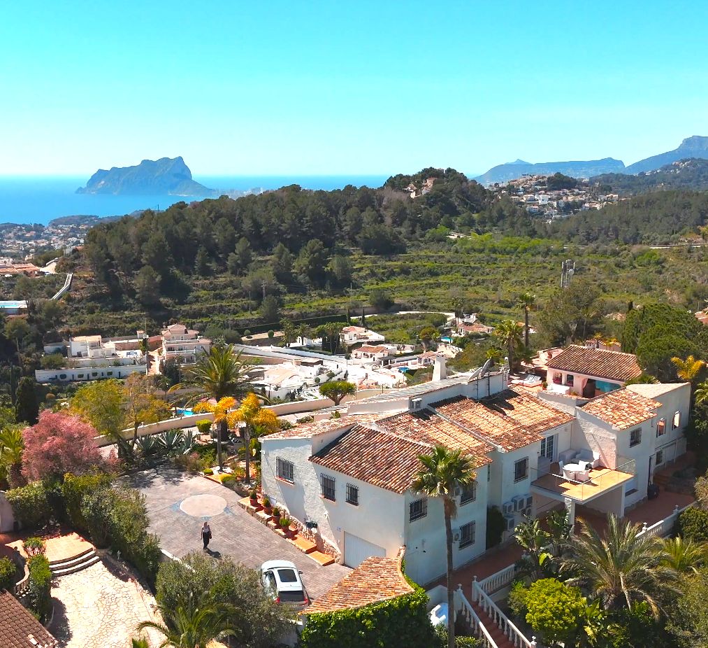 Aerial view of the multi-level Mediterranean villa featuring terracotta roofs, lush gardens, and a panoramic backdrop of the sea and Peñón de Ifach.