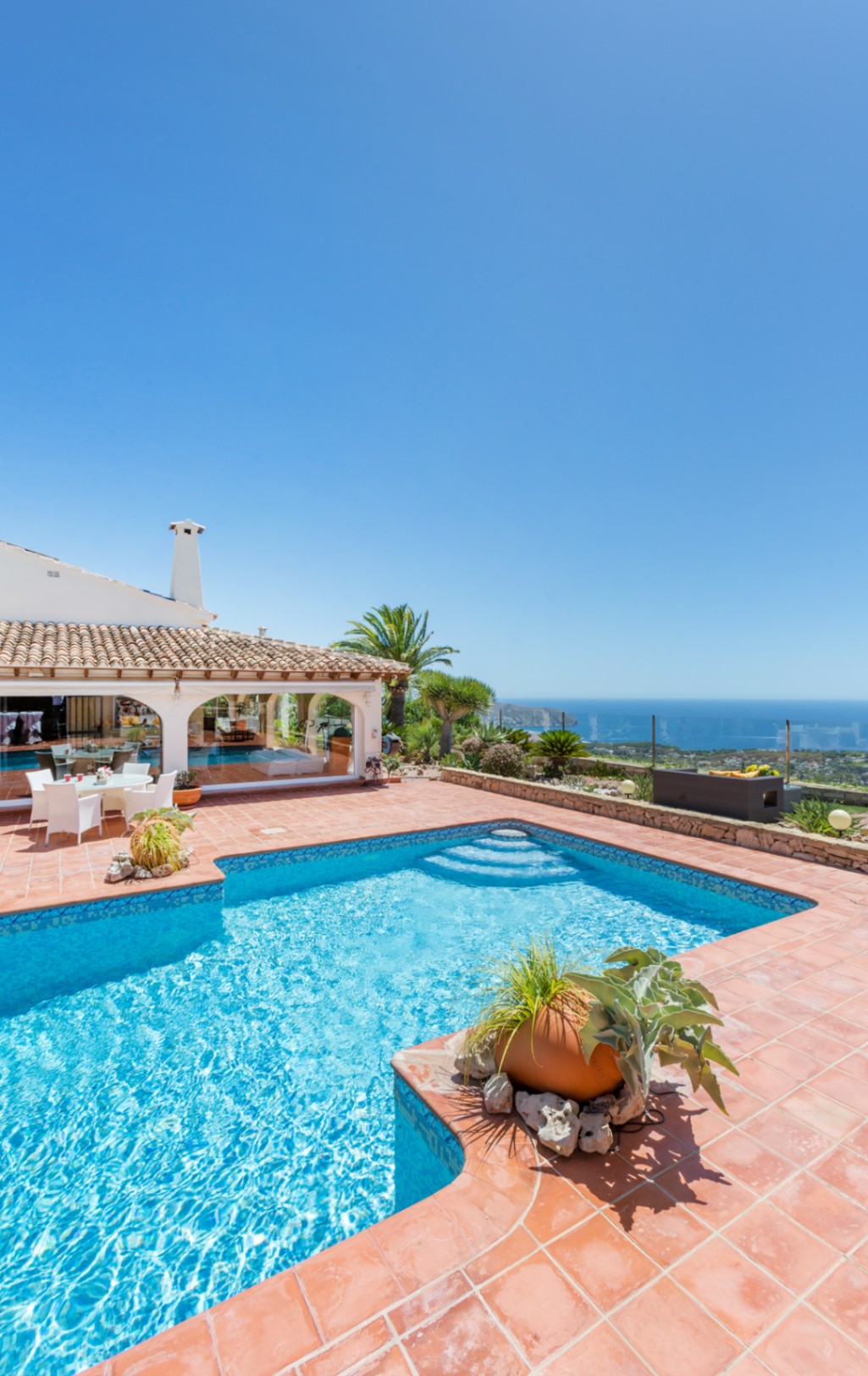 Outdoor swimming pool with blue mosaic tiles and terracotta terrace, offering panoramic views of the Mediterranean Sea and the coastline.
