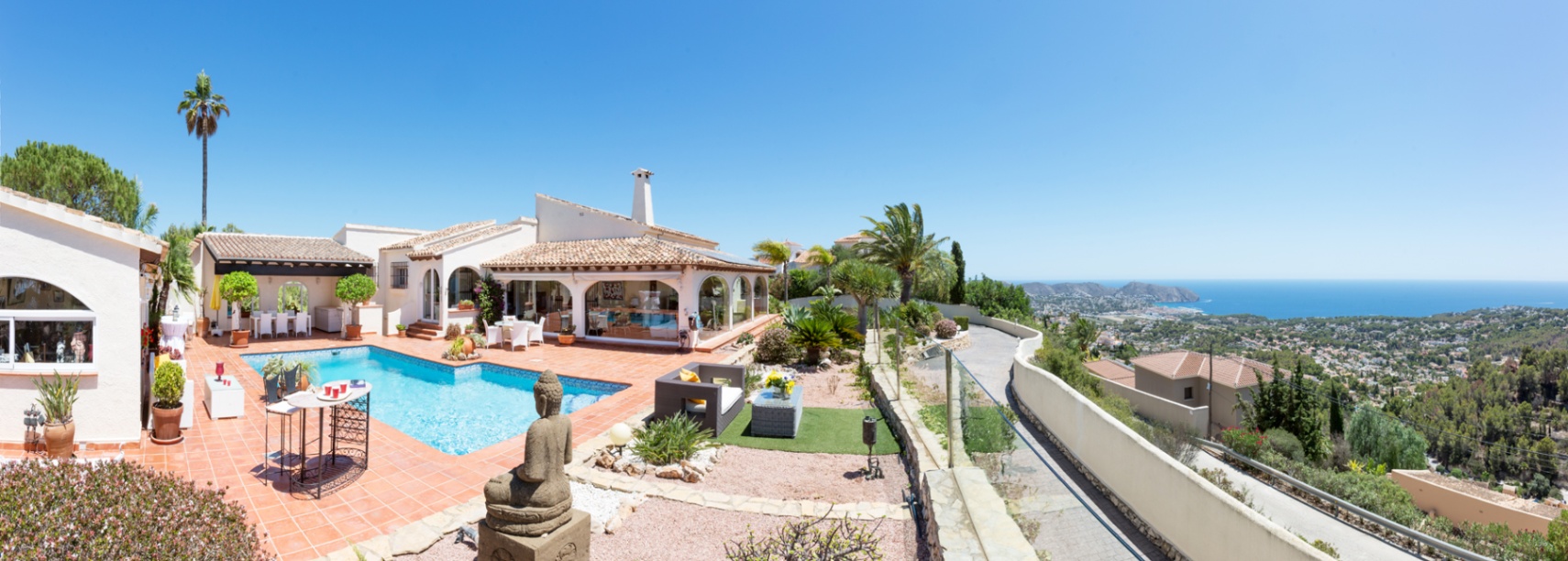 Panoramic terrace with terracotta tiling, a private pool, and a decorative Buddha statue, overlooking the Mediterranean Sea and coastal landscape.